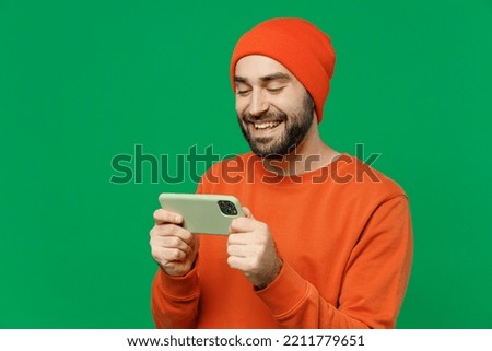 Young gambling happy cool man 20s wear orange sweatshirt hat using play racing app on mobile cell phone hold gadget smartphone for pc video games isolated on plain green background studio portrait. Royalty-Free Stock Photo #2211779651