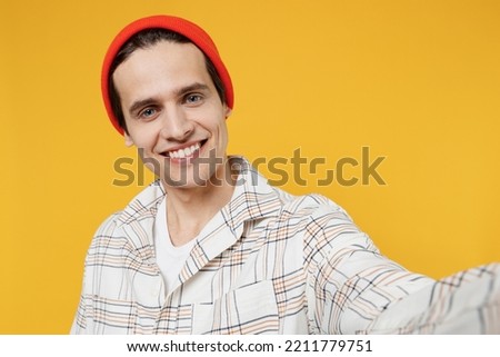 Close up young smiling happy cheerful caucasian man 20s wearing white casual shirt orange hat doing selfie shot pov on mobile phone isolated on plain yellow background studio People lifestyle concept
