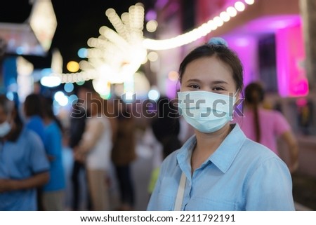 Asian women wearing masks Go to an event that is held at night. It is decorated with many light bulbs, creating a circular bokeh in the background.