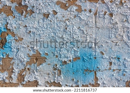 Cracked grungy wall texture background, old broken ragged paint layers. Rough peeling wall stained in white and light blue colors. Bad shabby wall close-up. Wallpaper, template, and design concept.