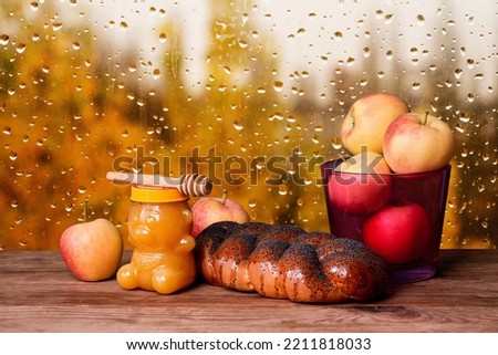 Jar with honey, braided bread and apples on windowsill with rainy autumn view