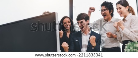 A team of exclusive diversity businesspeople are gathered together in an office, excitedly watching their accomplishment on a laptop computer. Idea for fostering strong teamwork in the workplace.