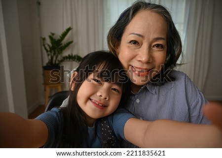 Old grandma and her little preschool granddaughter holding cellular taking self-portrait picture.