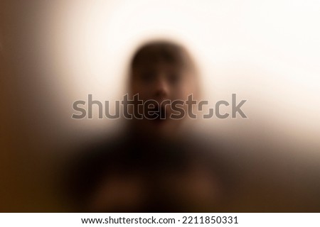 Horror ghost woman behind the matte glass. Grunge, blurred Halloween festival background.