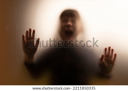 Horror ghost girl screaming behind the matte glass. Halloween festival concept. Grunge, blurred background.