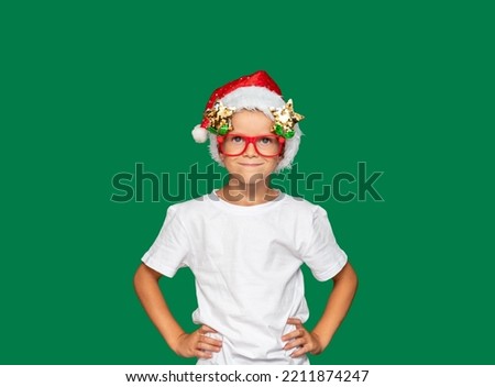 Boy in Santa Claus hat and glasses. Green background with space for text. Selective focus. Picture for articles and advertisements about children, holidays, Christmas.
