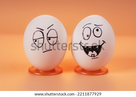 Two eggs with painted funny faces representing people in worried and carefree emotional states. Close up view on beige background