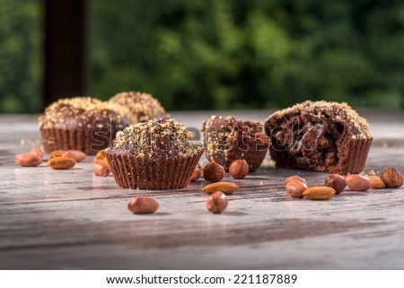 Close-up picture of four chocolate cupcakes one of them broken decorated with almonds and hazelnut on wooden table in cafe with selective focus only on two of the cupcakes with copy place