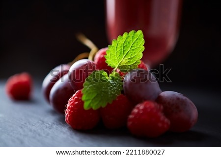 Grapes and raspberries and fresh smoothie in a glass. Dark background. Close up. 