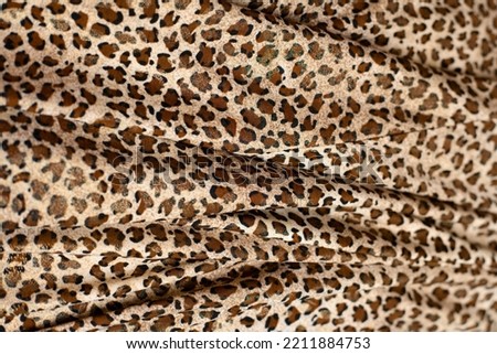 Wavy beautiful fabric with wild animal leopard or cheetah print on it, popular fabric among women with spots, leopard skin, copy space, close up
