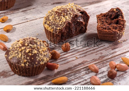 Close-up picture of two tasty chocolate cupcakes decorated with almonds and hazelnut on wooden table in cafe, with selective focus only on one broken cupcake, with copy place