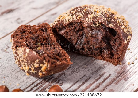 Close-up picture of tasty broken chocolate cupcake decorated with almonds and hazelnut on wooden table in cafe with copy place