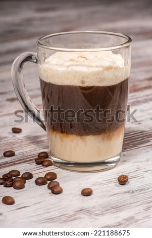 Close-up picture of tasty three-tiered milk coffee dessert standing on the wooden table in cafe decorated with grains of coffee with copy place