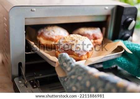 a woman cook takes out sweet Polish donuts from the oven Royalty-Free Stock Photo #2211886981
