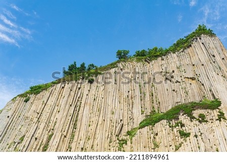 top of columnar volcanic basalt cliff against the background of the sky with clouds