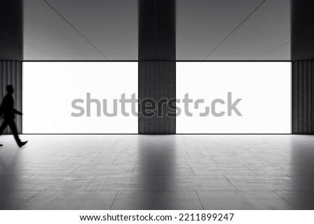 Front view on two blank white glowing boards with place for your logo or text in empty dark hall with walking by man silhouette, mock up