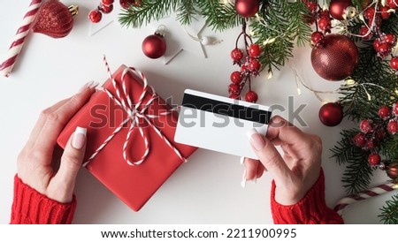 Hands of woman in red sweater holding credit card and gift box on white background close-up,top view,flat lay,copy space.Christmas and New Year online shopping,credit card payment.Buying gifts online