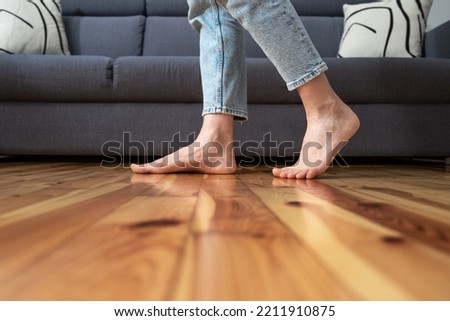 cropped shot of female legs walk barefoot on wooden warm floor near couch in living room at home, heating concept Royalty-Free Stock Photo #2211910875