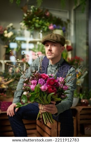 Caucasian male in peaked cap and vintage clothes from 10s holding beautiful bouquet of red and violet flowers. Mother's Day or Valentine's Day concept. High quality vertical image