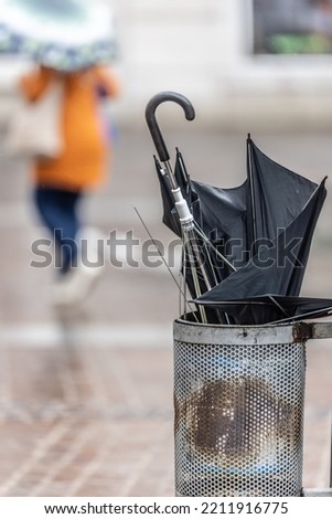 Umbrella damaged by the wind gust is thrown into a street bin on a rainy autumn day.