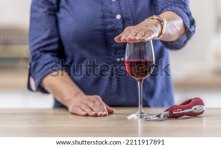 Detail of a female hand holding palm over a glass of red wine as a sign of refusal to drink.