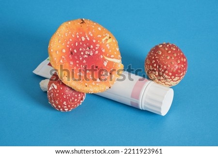 tube of cream or ointment and fly agaric on a blue background, medicinal properties of fly agaric for cosmetics and drugs