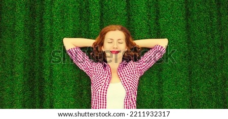 Portrait of happy smiling young relaxing woman lying on the grass background in park