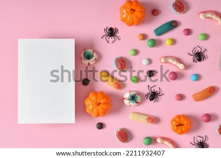 Kraft envelope with empty paper on the background of various sweets on a pink background. Happy Halloween. A place to copy. Flat position, top view