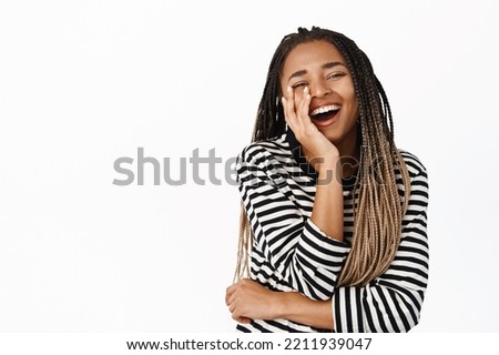 Portrait of african american woman laughing and smiling, touching her face, expressing genuine happiness and joy, standing over white background Royalty-Free Stock Photo #2211939047