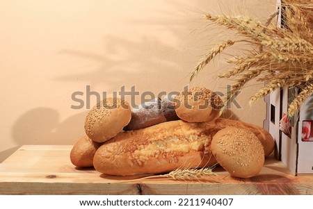 Freshly baked homemade bread, french sourdough baguette with crispy crust and ears of rye and wheat on wooden background with place for text, modern bakery concept,