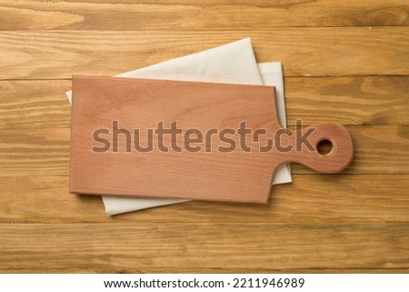 Cutting board with towel on wooden background, top view.