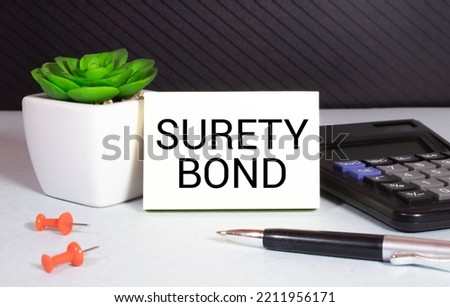 On the desktop there are reports, notepads, a calculator, a cash and a yellow sticker with the text SURETY BOND. Business concept Royalty-Free Stock Photo #2211956171