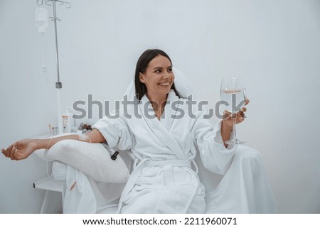 Beautiful woman in white bathrobe drink water during medical procedure in beauty clinic Royalty-Free Stock Photo #2211960071