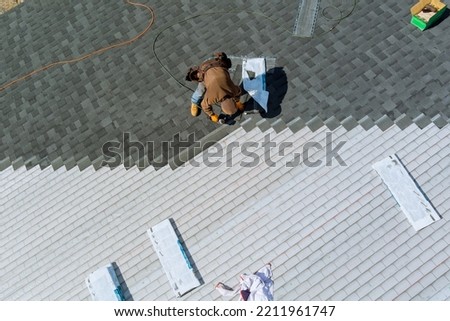 Aerial view of worker nailing new roof shingles with bitumen using an air hammer Royalty-Free Stock Photo #2211961747