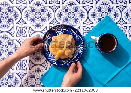 Traditional Mexican bread of the dead also known as "Pan de Muerto" on traditional Mexican tableware on traditional blue tile background.