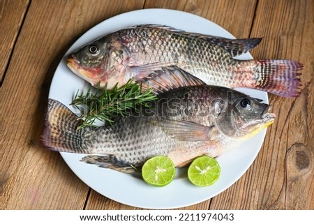 Tilapia with white plate with rosemary lemon lime on wooden background, Fresh raw tilapia fish from the tilapia farm - top view Royalty-Free Stock Photo #2211974043