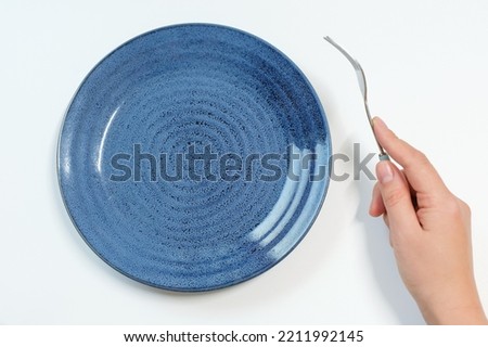 Empty plate and female hand with fork on white background close-up top view. Royalty-Free Stock Photo #2211992145