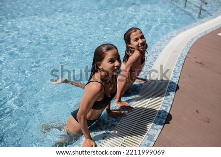 Back view of a two friends swimming in the pool, basking in the sun during the bathing break. girls get sunbathing, relaxing in the vacation at the hotel against the background pool with blue water