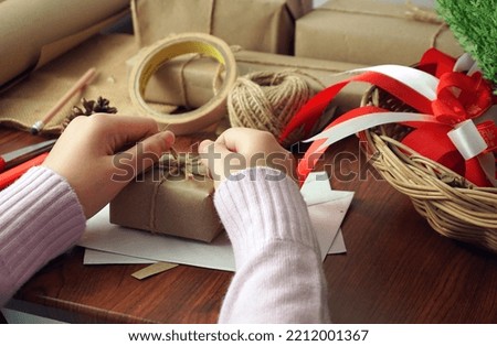 Woman's hand hemp rope is tied to a handmade gift box on a wooden table. Get ready for the festival of love and happiness. surrounded by equipment for made gift boxes