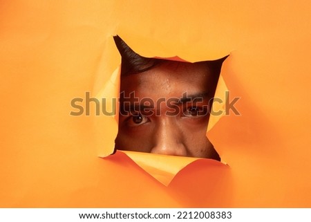 mysterious facial expression behind the orange torn paper