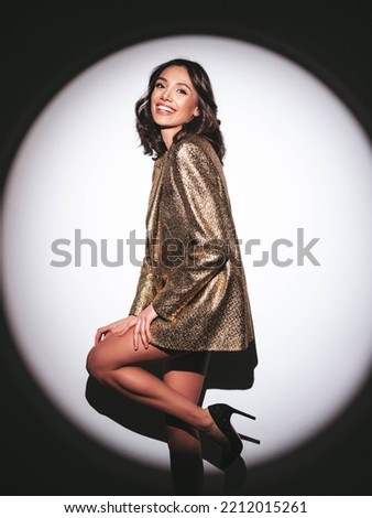Young beautiful smiling brunette female in trendy evening golden jacket. carefree woman posing near silver shiny tinsel wall in studio .Fashionable model with bright makeup Royalty-Free Stock Photo #2212015261