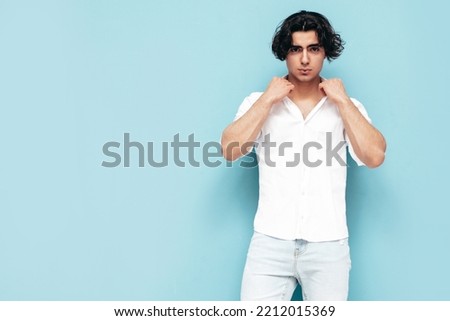 Portrait of handsome confident stylish hipster lambersexual model.Man dressed in summer white shirt and jeans clothes. Fashion male isolated in studio. Posing near blue wall Royalty-Free Stock Photo #2212015369