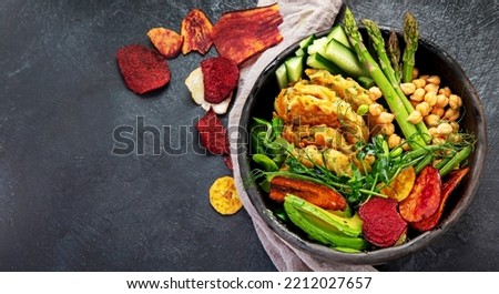 Vegan buddha bowl. Bowl with  vegetables, Zucchini fritters and vegetables chips. Dark background. Healthy eating concept. Top view, copy space