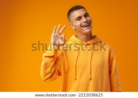 Happy young man gesturing OK sign against yellow studio background
