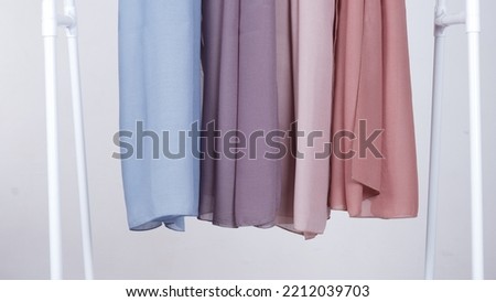4 hijabs hanging on a shelf. white background.