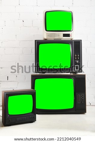 Four vintage green screen televisions with a white brick background.