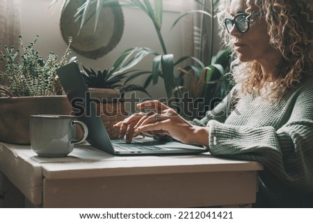 Professional woman working at home on laptop writing with concentrated expression. Modern female people using computer in indoor online leisure activity. Shopping or business smart work job freelance Royalty-Free Stock Photo #2212041421