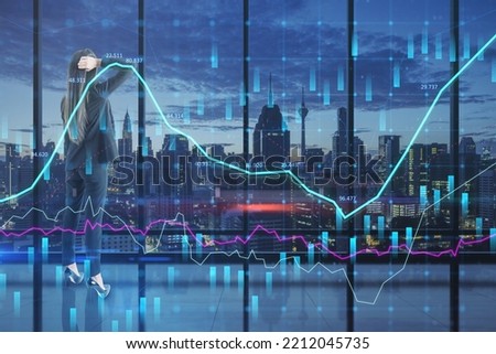 businesswoman looking at glowing candlestick forex chart hologram on blurry panoramic office window frame with blurry night city view. Stock, investment, market and money concept. Double exposure