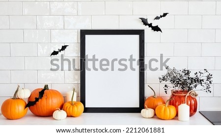 Black picture frame mockup with pumpkins, Halloween home decor, vase of flowers on table in scandinavian kitchen interior. Happy Halloween poster design.