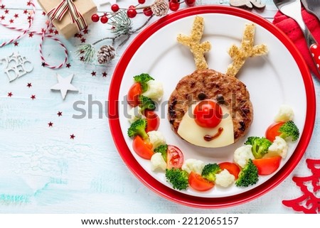 Fun Food for Kids - Christmas reindeer shaped chicken burger decorated with cheese and tomatoe served with healthy steamed vegetables like broccoli and cauliflower
